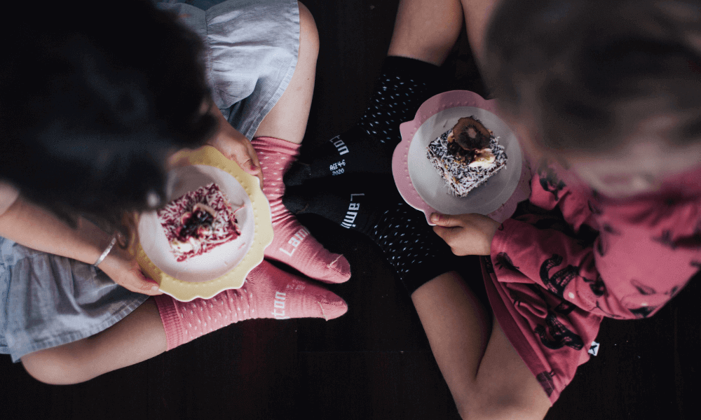 Kids enjoying homemade Chocolate Lamingtons  while sitting on the floor.