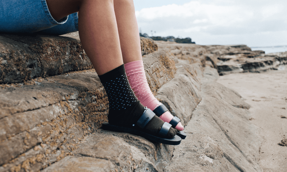 Person sitting on rocks at the beach wearing odd socks while pondering what to do with odd socks.